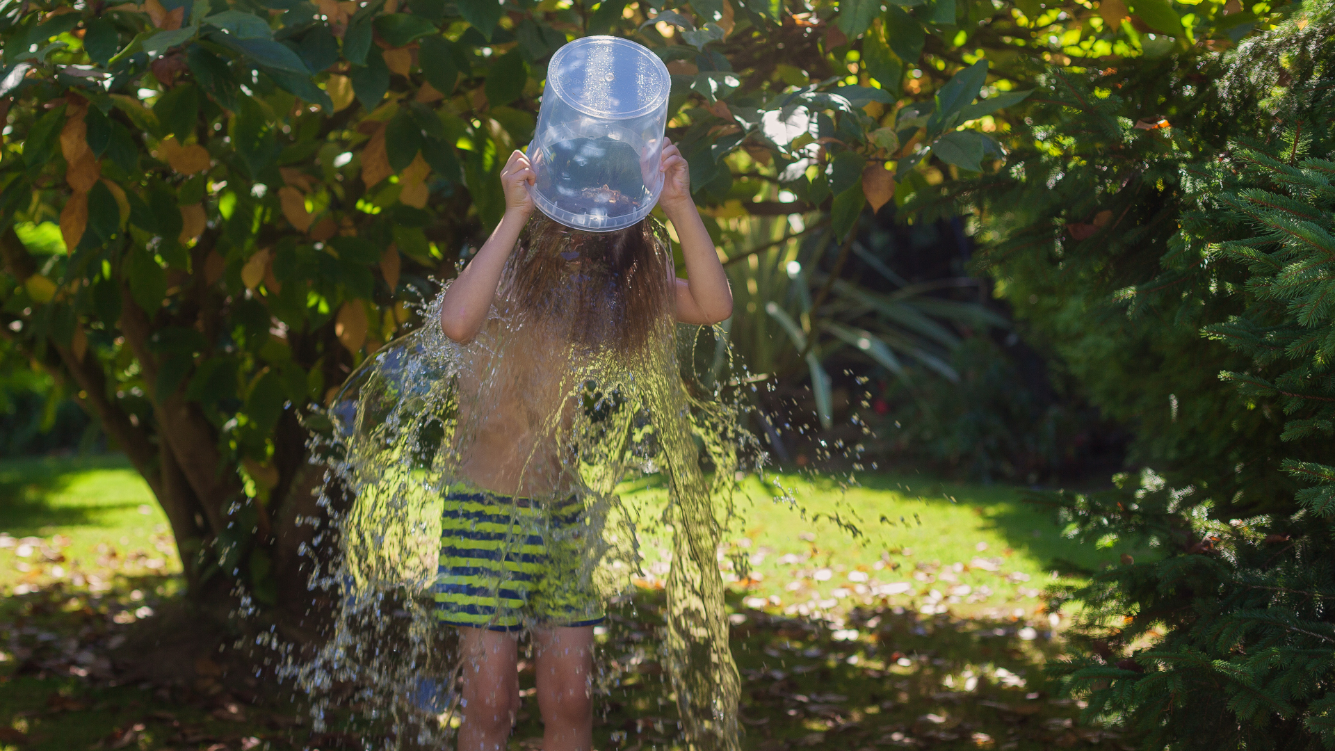 Un niño en traje de baño arroja un balde de agua sobre su cabeza