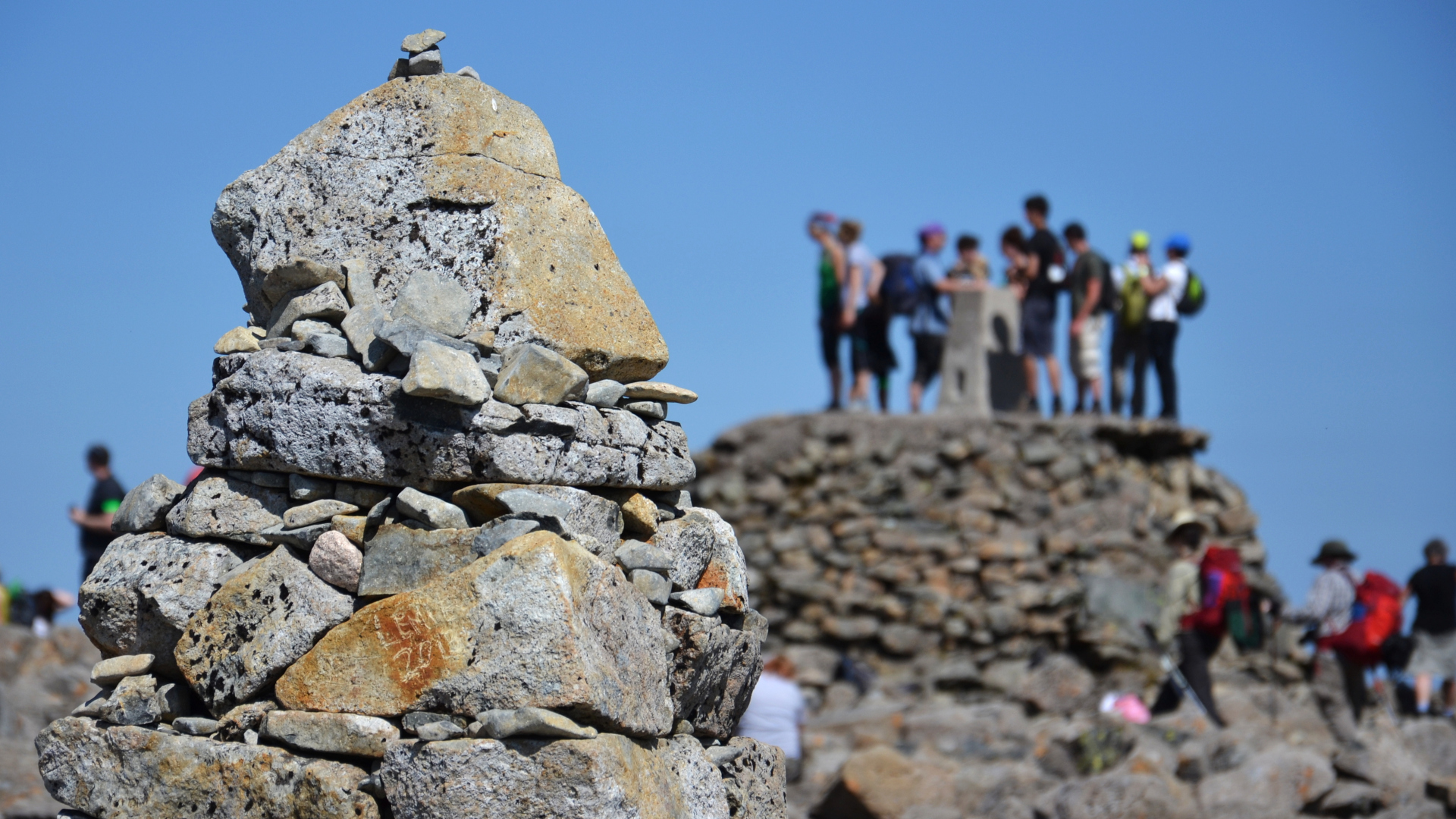 Mojón de roca en la cumbre de Ben Nevis con excursionistas en la distancia