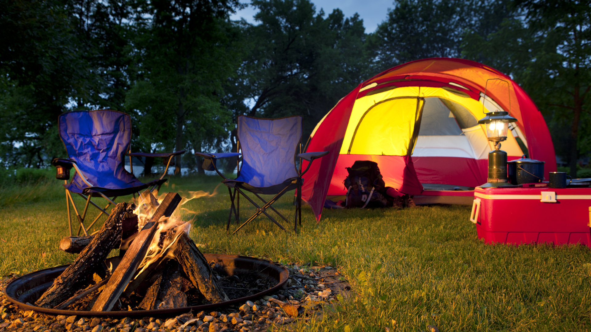 Un camping por la noche con dos sillas azules y una fogata