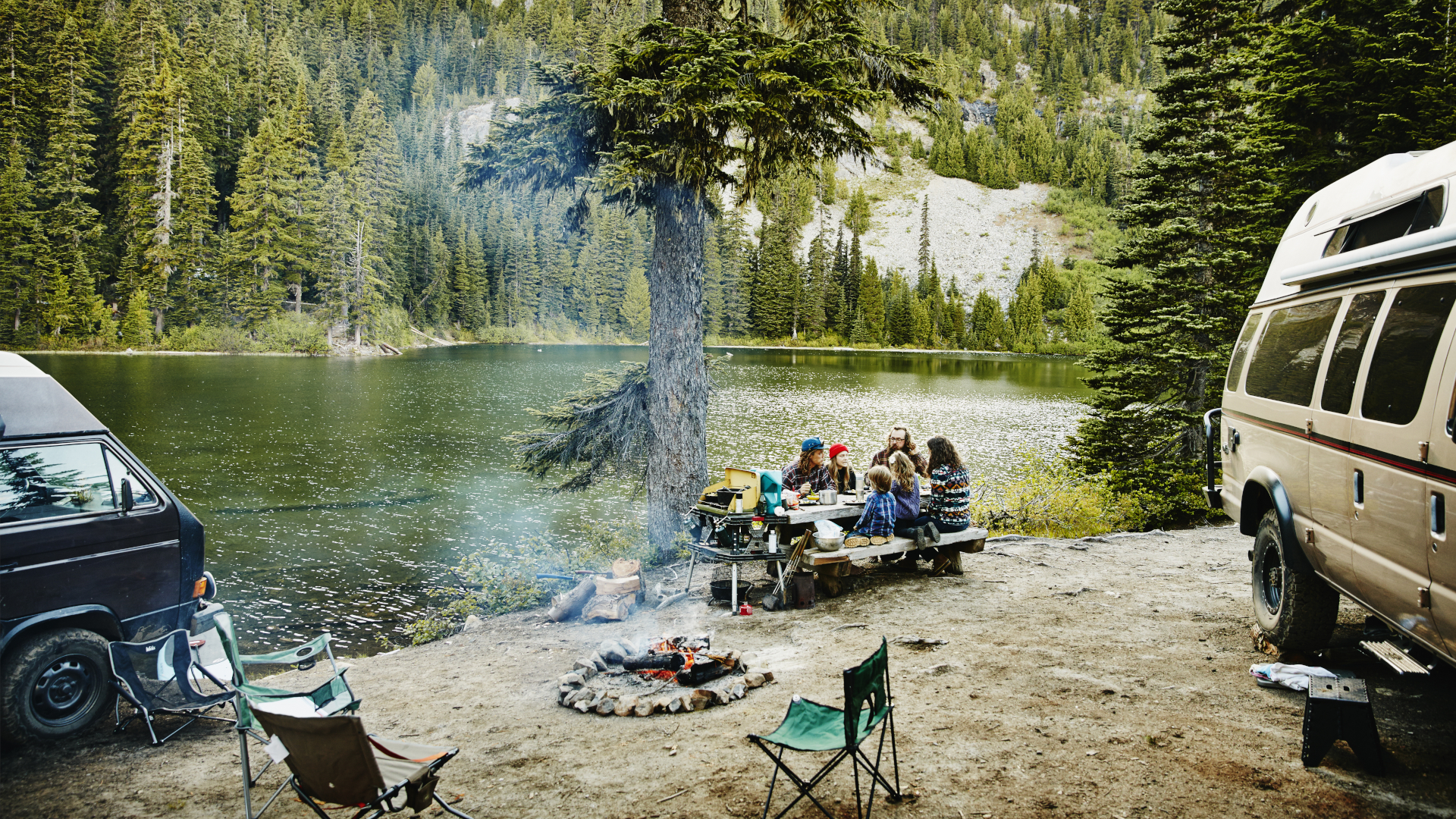 Amigos compartiendo una comida mientras acampan junto al lago