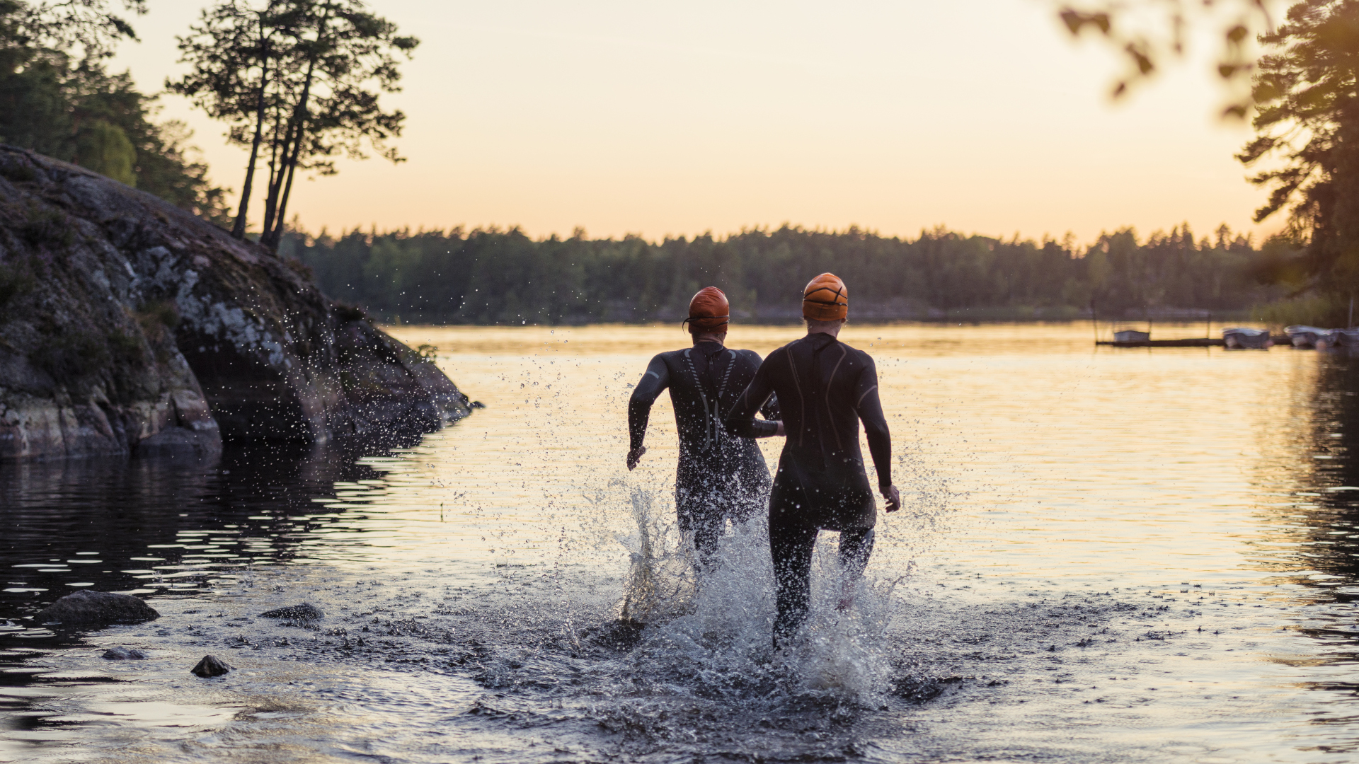 Dos personas en trajes de neopreno corriendo hacia el agua al atardecer