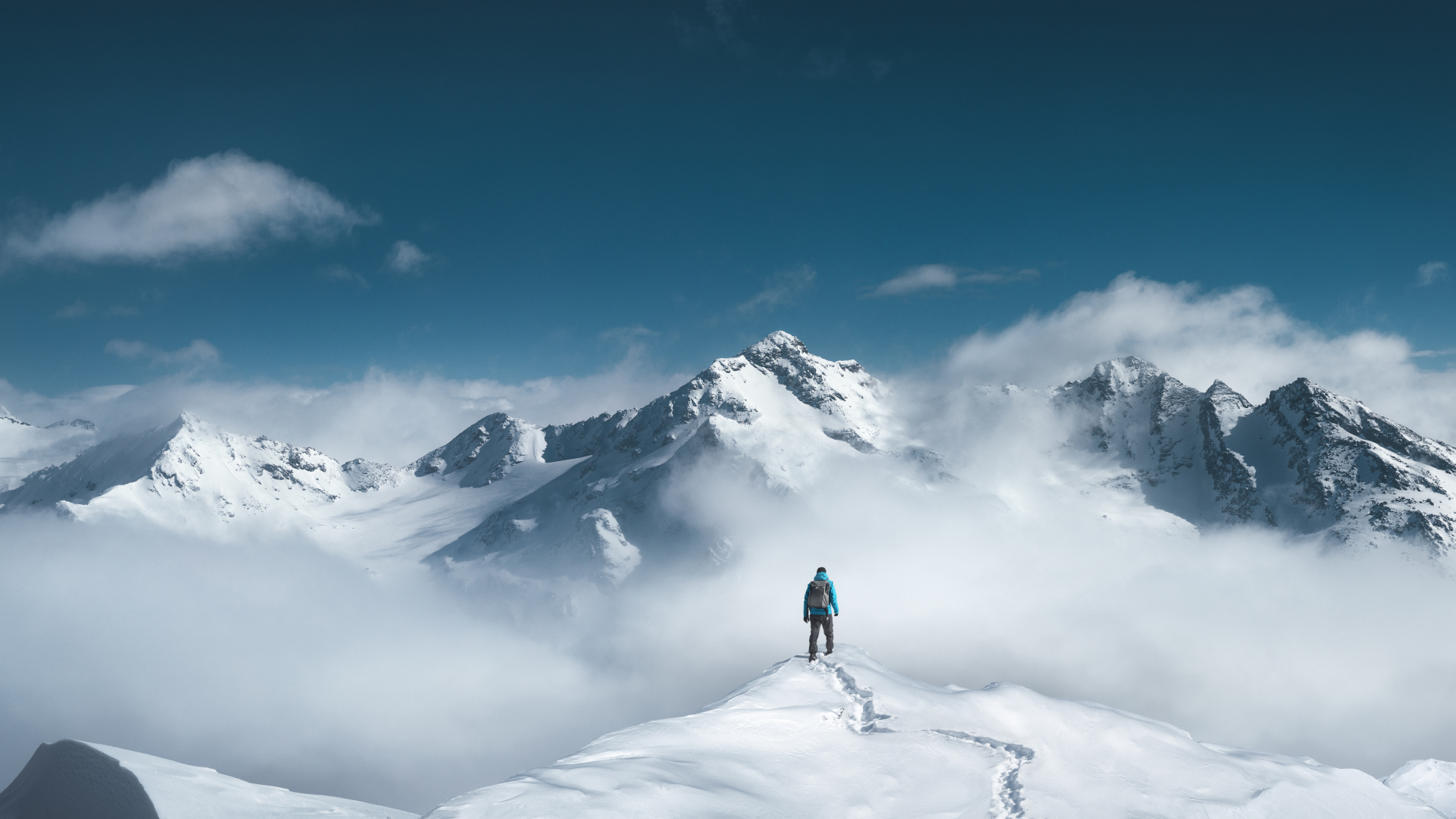 Un excursionista de pie en la cima de un pico de montaña cubierto de nieve