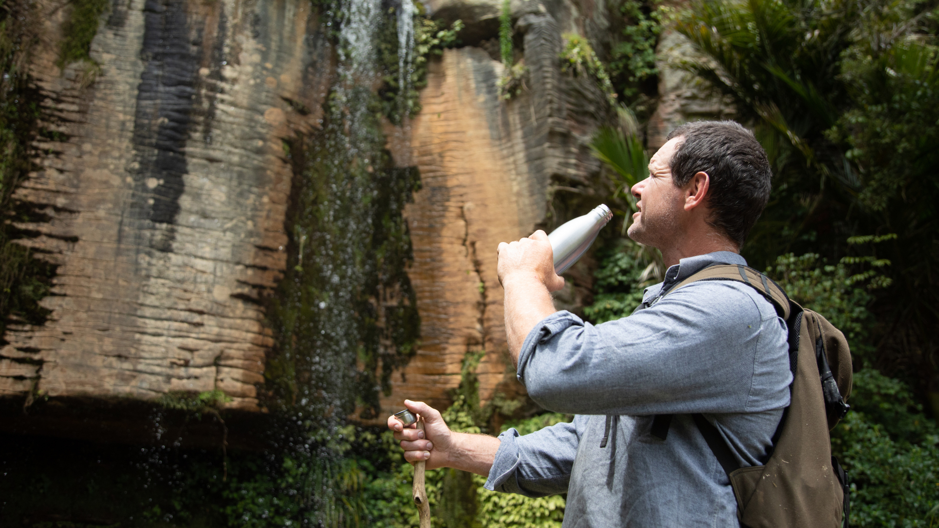 Un excursionista bebe agua mientras mira una cascada.