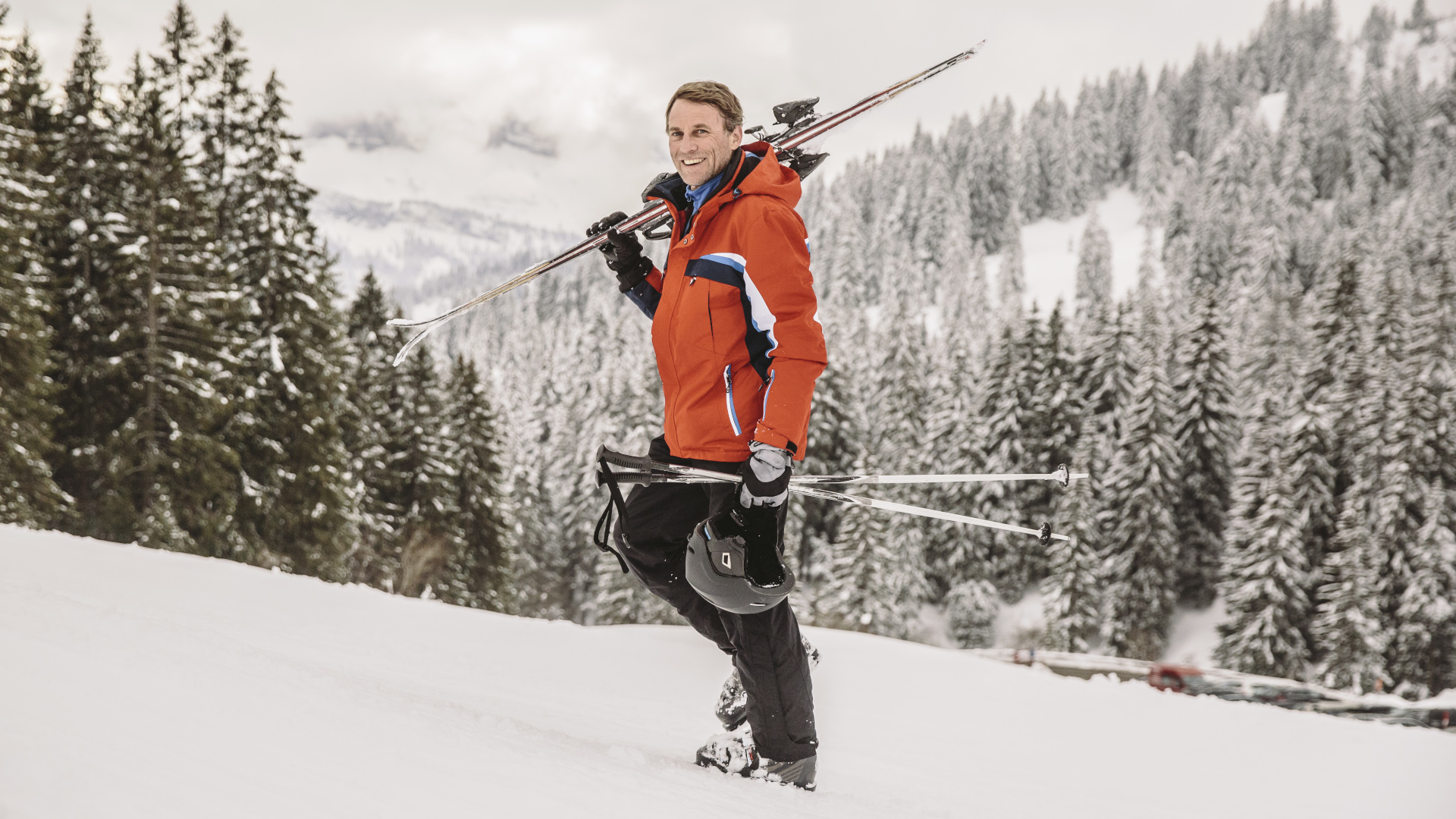 Un esquiador con una chaqueta roja lleva su equipo de esquí cuesta arriba