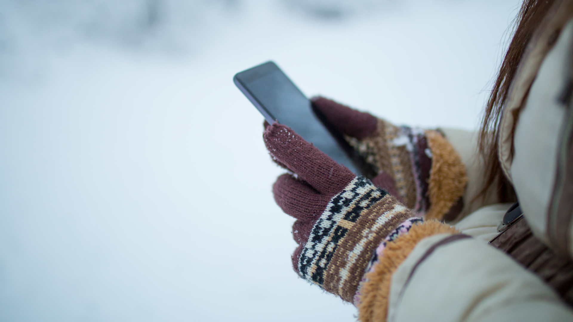 Manos femeninas sosteniendo un celular al aire libre en la nieve.