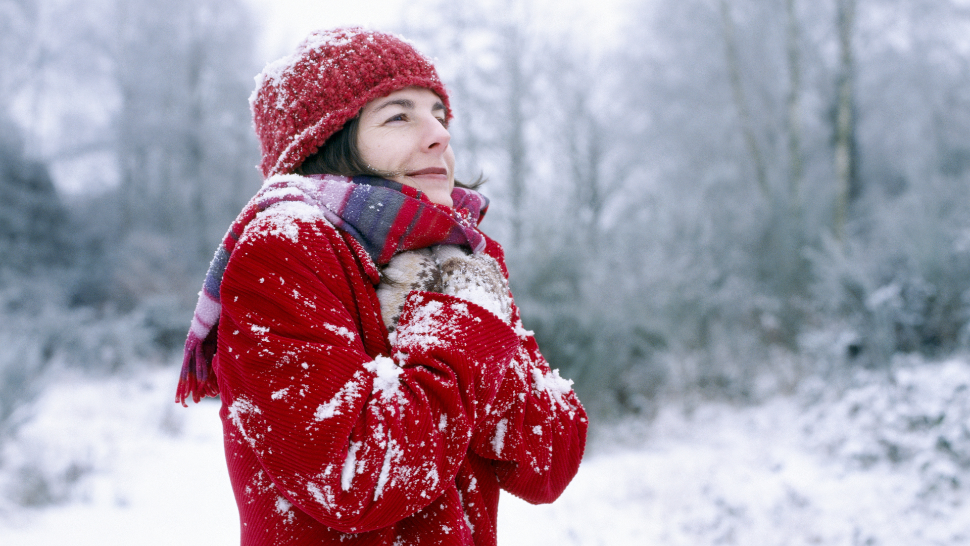 Una mujer con un abrigo rojo tiembla en un paseo nevado