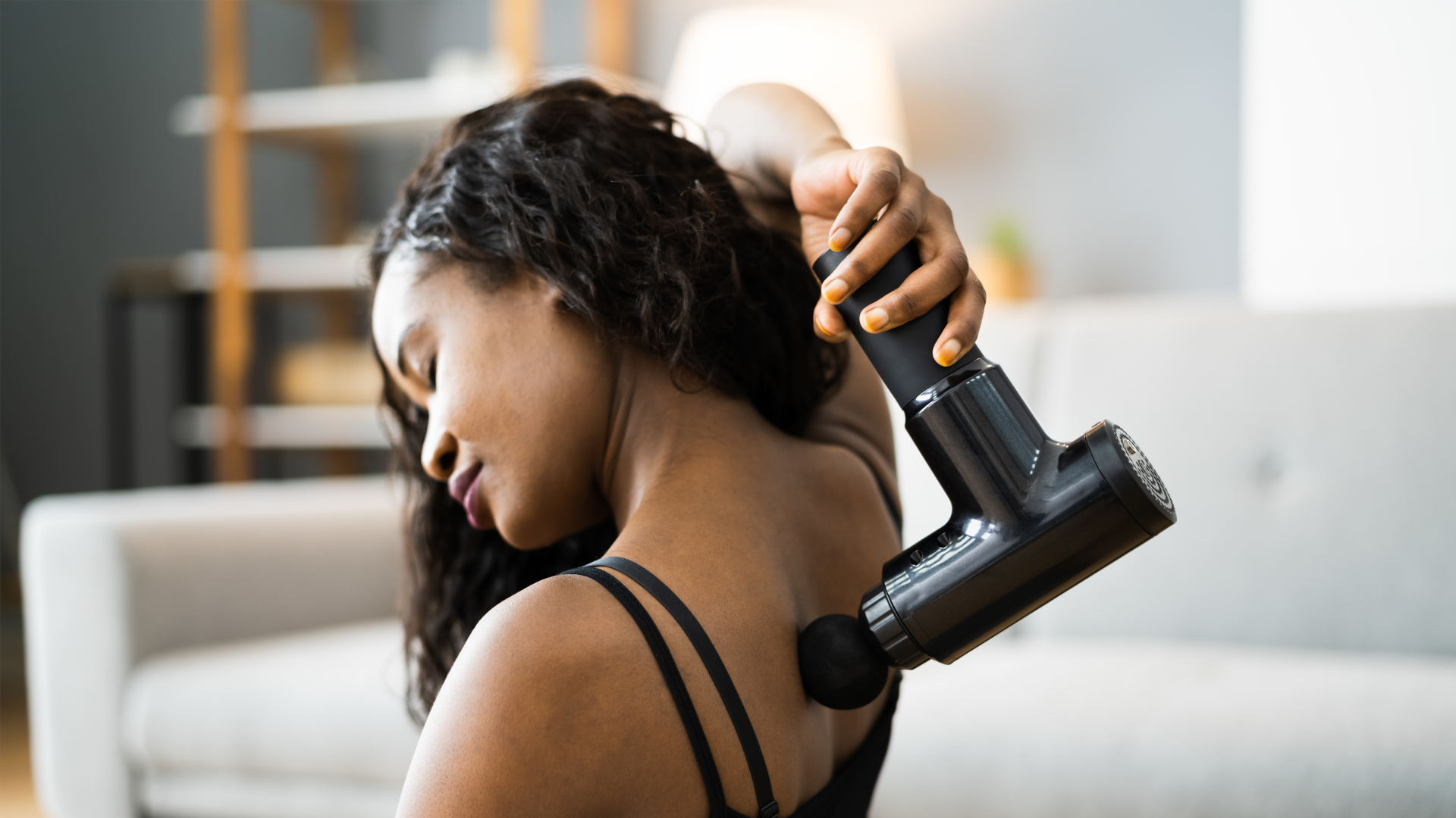 mujer usando pistola de masaje en el hombro