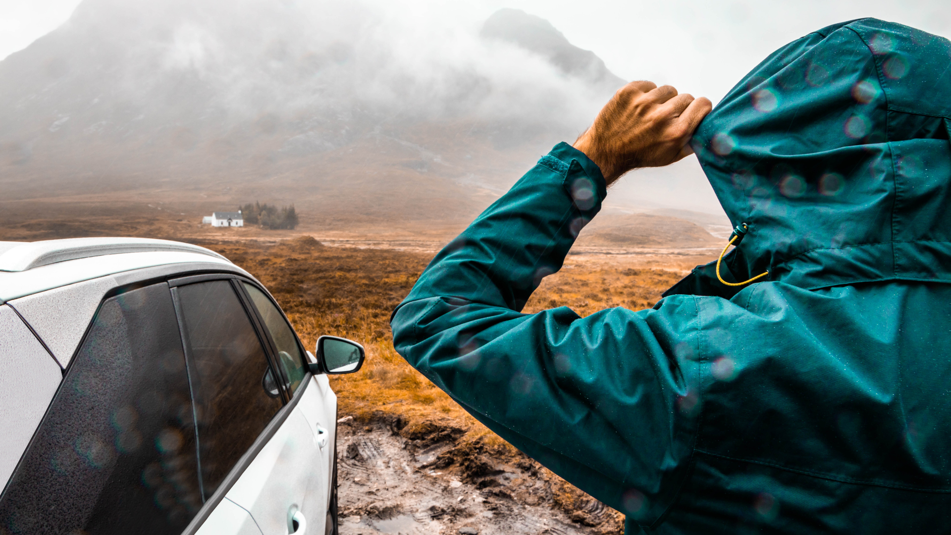 Un excursionista con impermeable se para junto a su auto mirando una montaña.jpg
