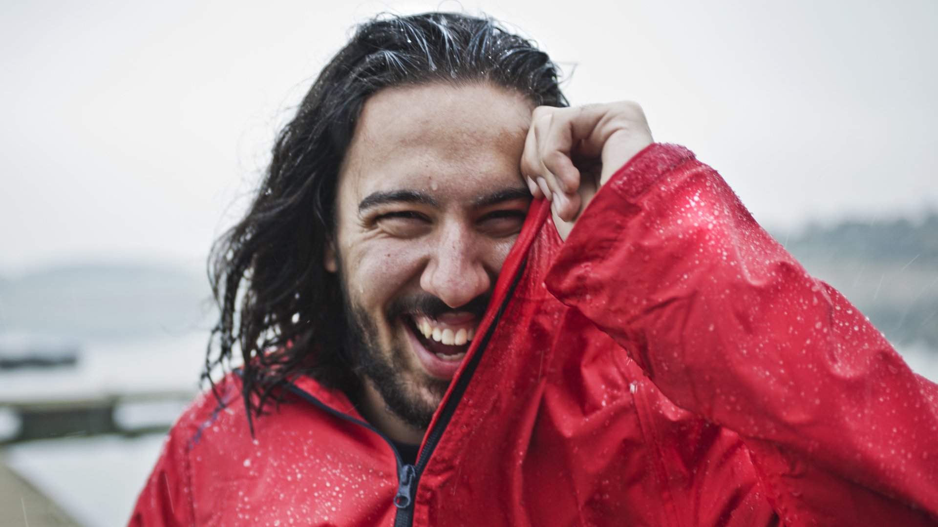 Un hombre con un impermeable rojo se ríe bajo la lluvia