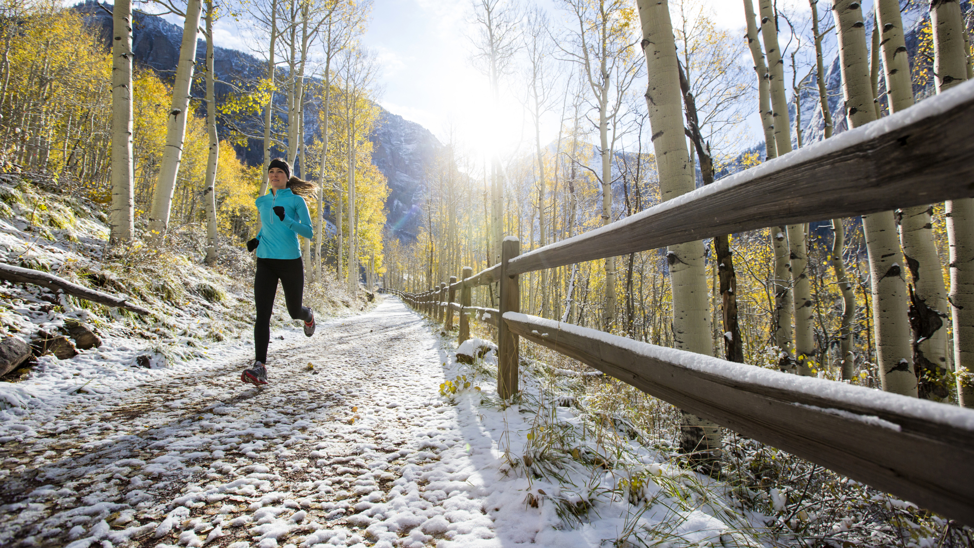 Una mujer corre por un sendero nevado en otoño con álamos amarillos detrás de ella