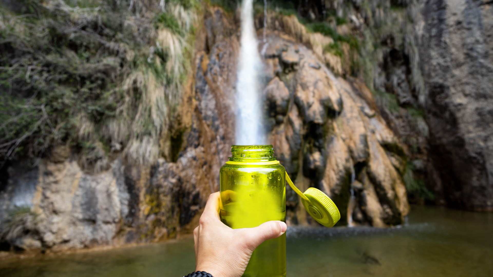 Un excursionista llenando una botella de agua de una cascada.