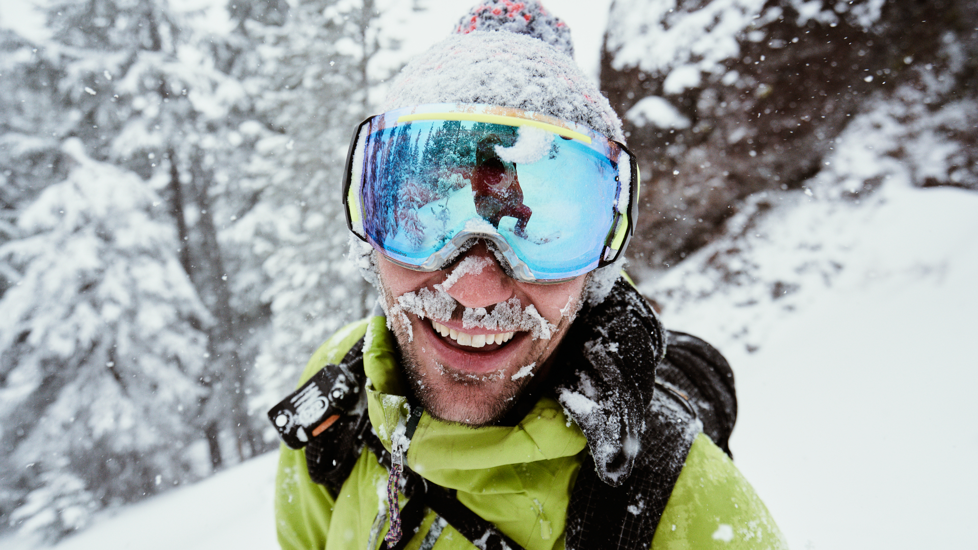 Un esquiador con gafas está sonriendo y cubierto de nieve en un día de polvo